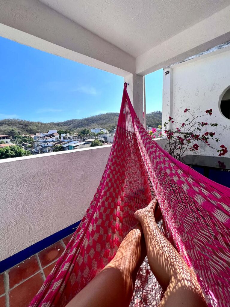 Feet in pink hammock on balcony in hotel