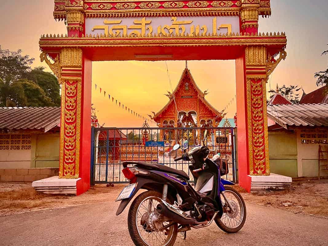 renting a scooter in thailand in front of a sunset temple
