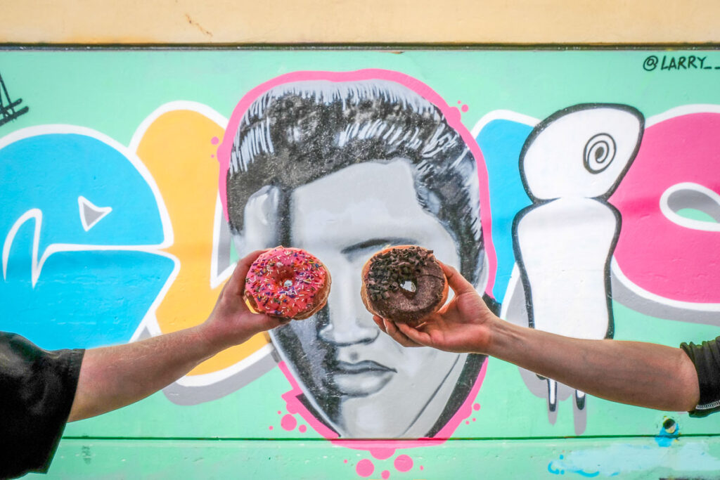 two donuts being held in front of elvis graffiti on a las vegas downtown donut food tour 