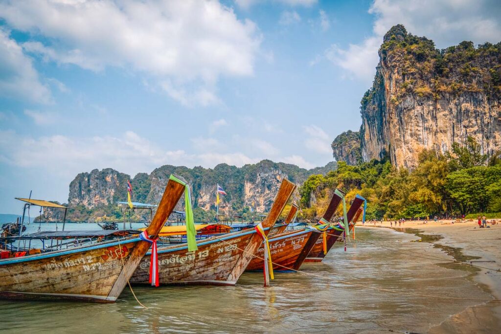 The iconic longtail boats of Krabi floating on calm waters of railay west beach, a popular phuket boat tour trip