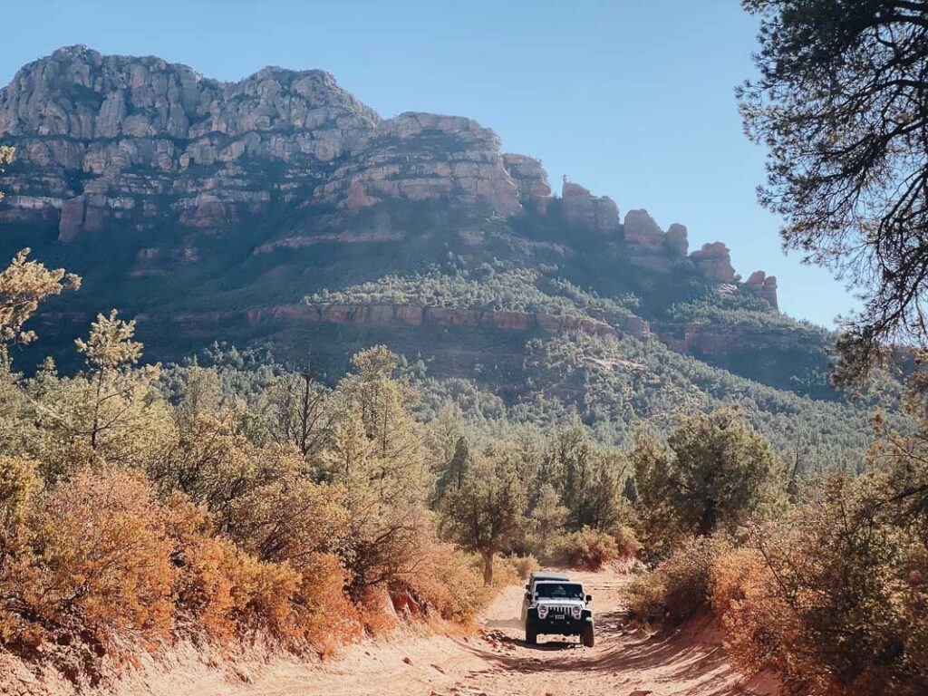 Jeep driving an off road trail in front of giant red rock formations