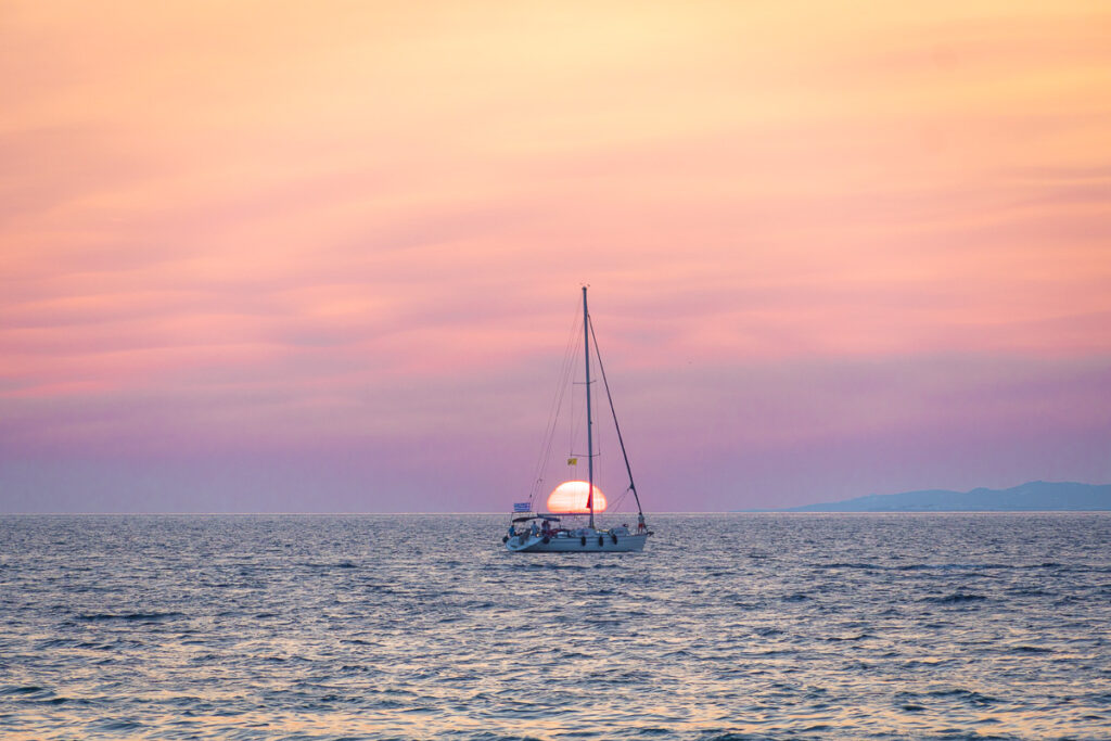 sailboat in front of setting sun in mykonos island greece