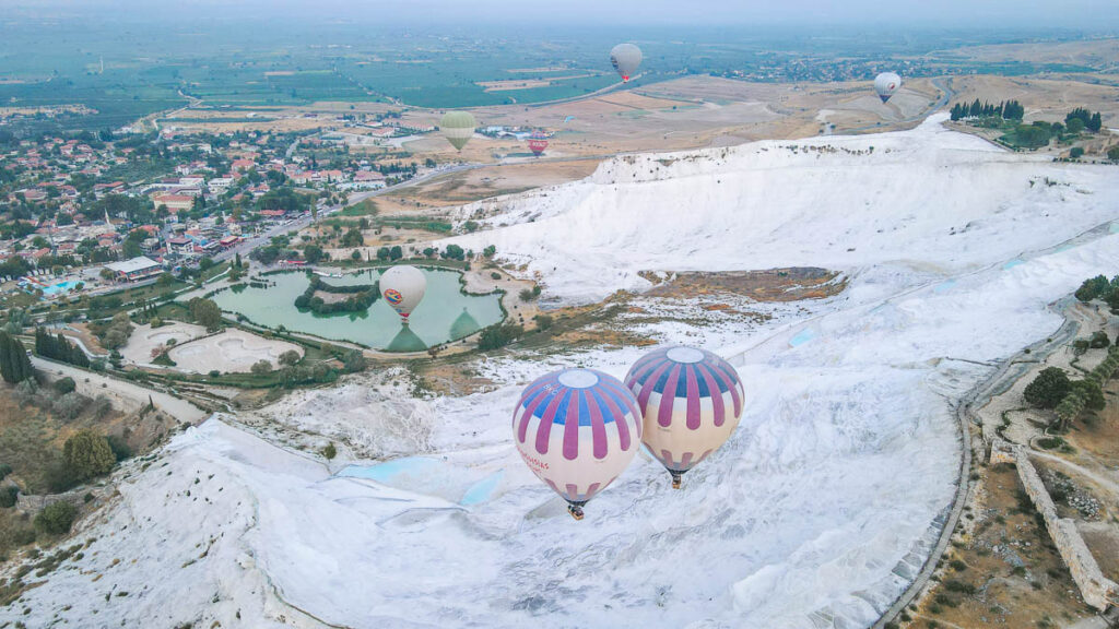 A magical perspective of Pamukkale's travertine pools and the surrounding landscape with many hot air balloons