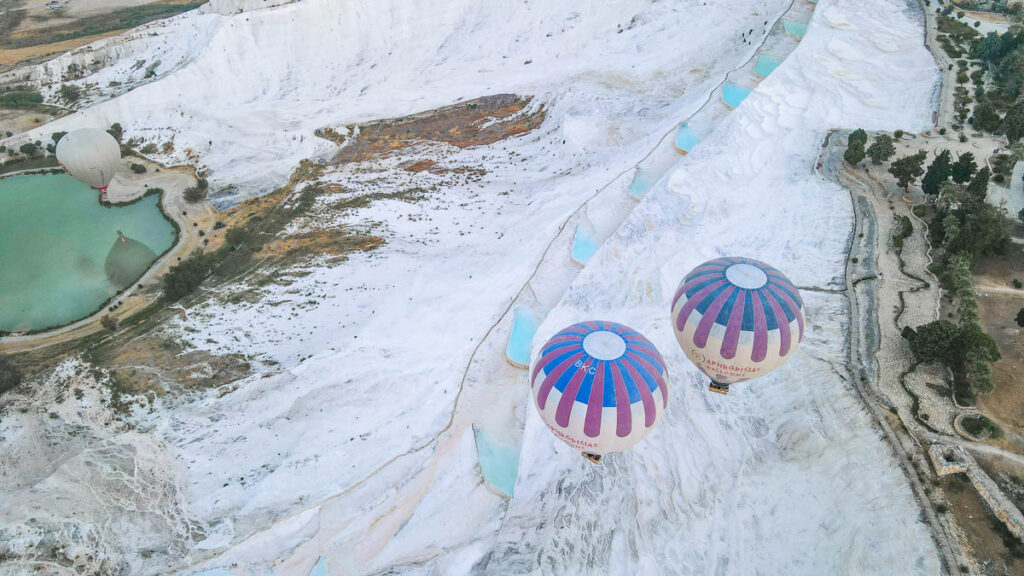 Gently floating above Pamukkale in a colorful hot air balloon, capturing the stunning terraces from above