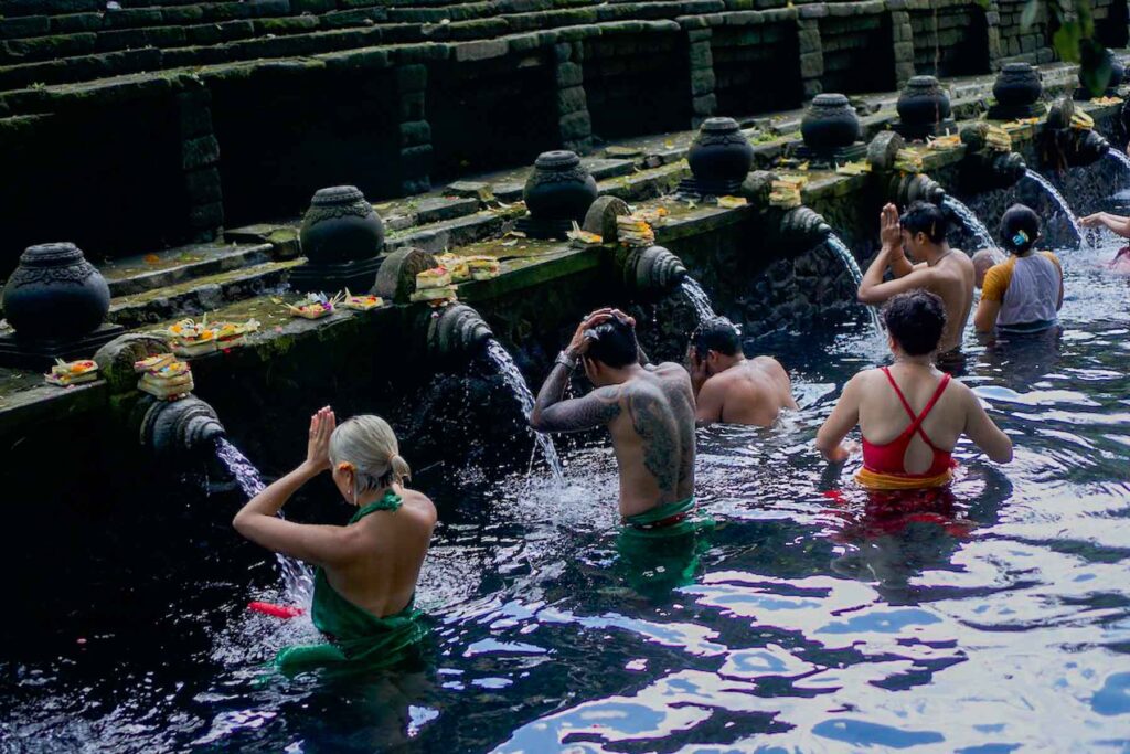 four people bathing themselves in the tirta empul cleansing ritual in the pools