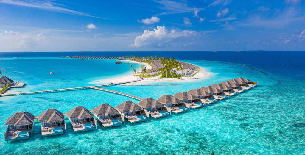 Maldives, Indian Ocean, aerial view of a tropical island resort with overwater villas arranged above crystal clear turquoise lagoon and white sand beach surrounded by coral reefs