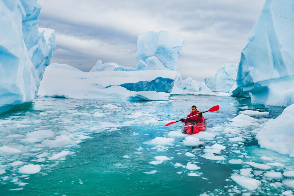 extreme tourism, winter kayaking in Antarctica, adventurous man paddling on sea kayak between icebergs
