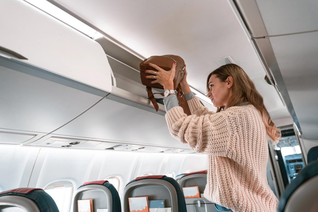Woman traveler putting luggage into overhead locker on airplane during boarding. High quality photo