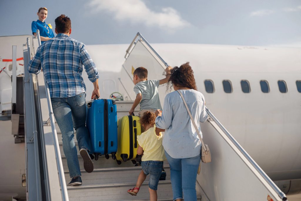 Back view of family of four getting on, boarding the plane on a daytime, ready for summer vacations. People, traveling, vacation concept
