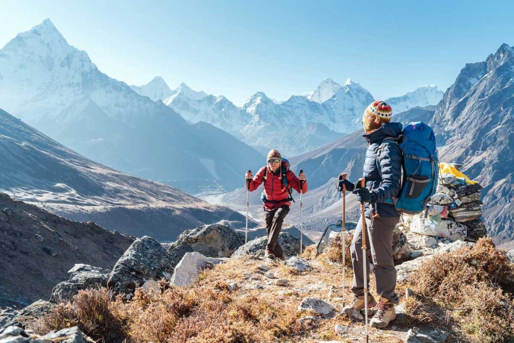 Couple following Everest Base Camp trekking route near Dughla 4620m. Backpackers carrying Backpacks and using trekking poles and enjoying valley view with Ama Dablam 6812m peak