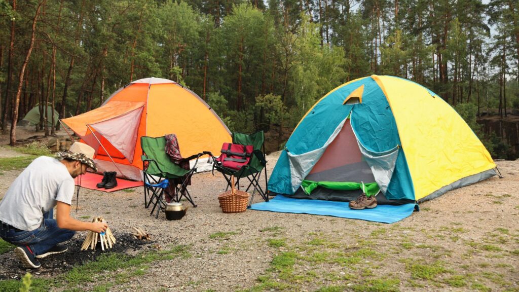 People, Camping Gear, Man lighting bonfire near camping tents in forest