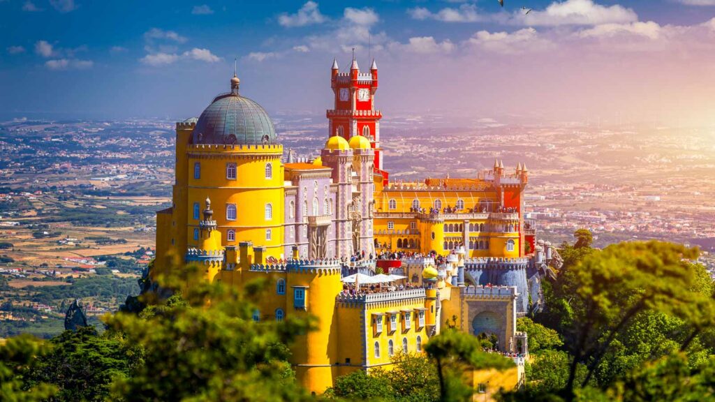 Famous historic Pena palace part of cultural site of Sintra against sunset sky in Portugal. Panoramic View Of Pena Palace, Sintra, Portugal. Pena National Palace at sunset, Sintra, Portugal.