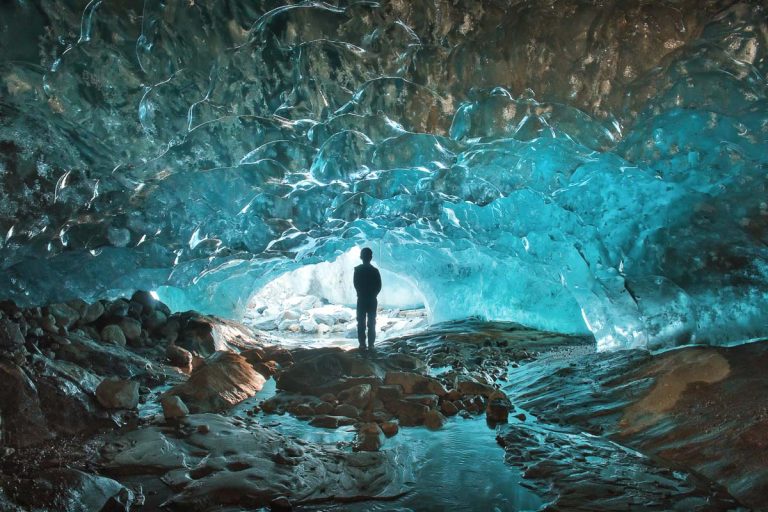 Russia, Karachay-Cherkessia, Dombay glacier ice cave with silhouette of man inside blue ice cavern