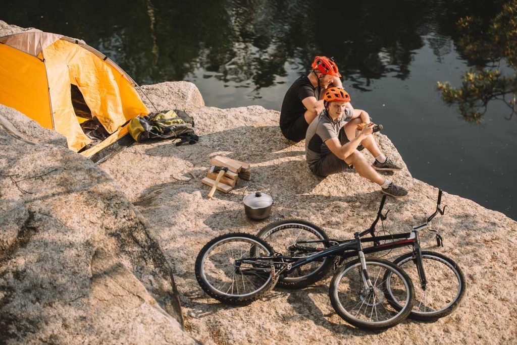 Trial bikers camping on rocky cliff above river with tent and bikes