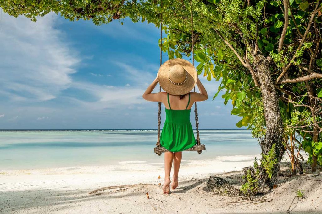 Woman in green dress swinging at tropical beach