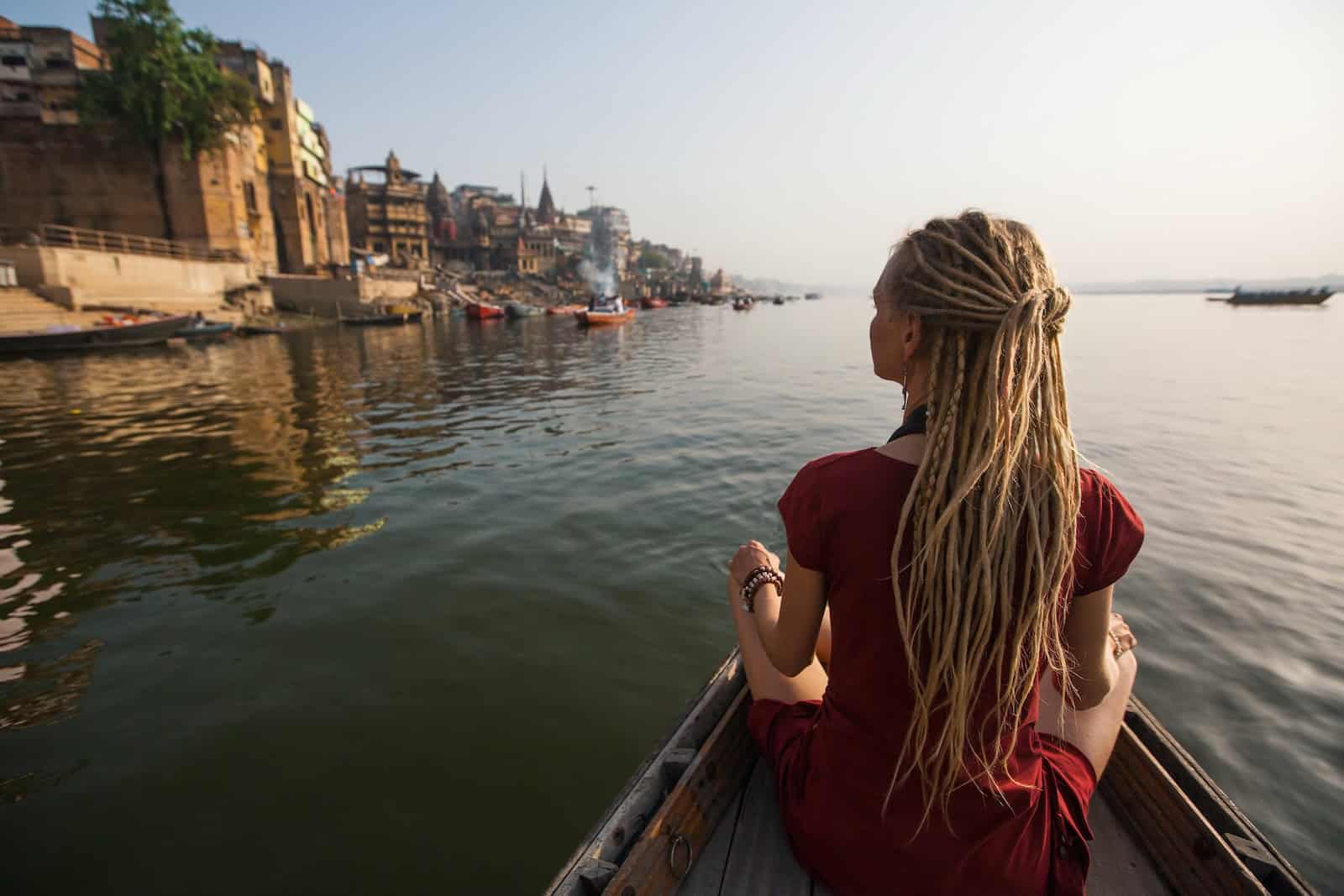 Young woman traveler with dreadlocks, on a boat glides through the water on the Ganges river along the shore of Varanasi, India.