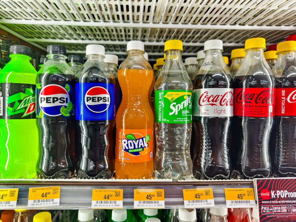 A variety of soda bottles with popular brands inside a chiller at a supermarket.