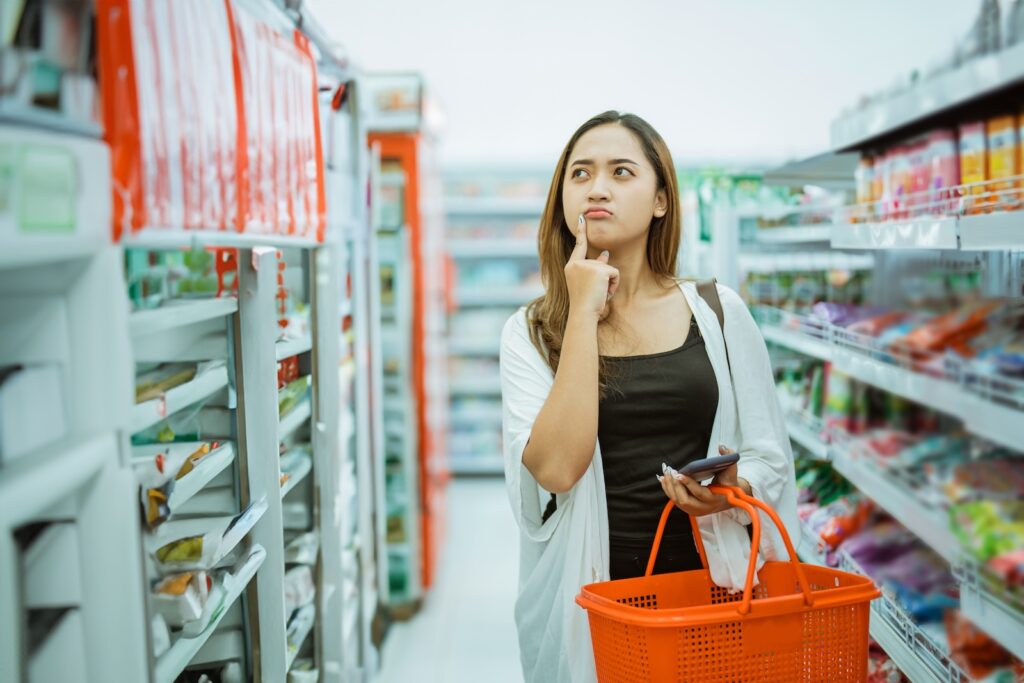 young woman thinking about what to buy while shopping carrying a cart at a minimarket