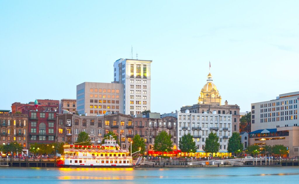 Savannah Georgia USA, skyline of historic downtown at sunset with illuminated buildings and steam boats