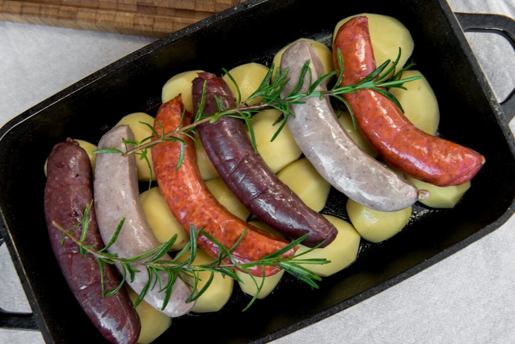 Raw sausages in the oven. Close-up of bowl with raw homemade blood sausage, pork sausage and chorizo in oven with potatoes. homemade traditional food.