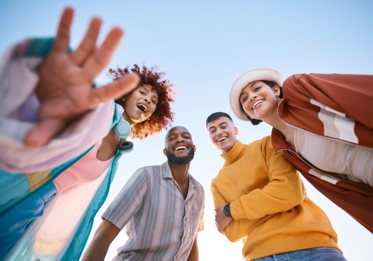 Portrait, smile and a group of friends on a blue sky outdoor together for freedom, bonding or fun from below. Diversity, travel or summer with happy men and women laughing outside on vacation.