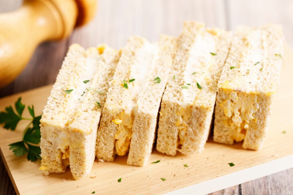 Egg sandwich, Egg salad with mayonnaise between slices of white bread, on wooden board. Closeup.