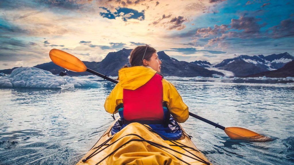 Woman paddle a canoe on an icy bay in Alaska exploring glaciers