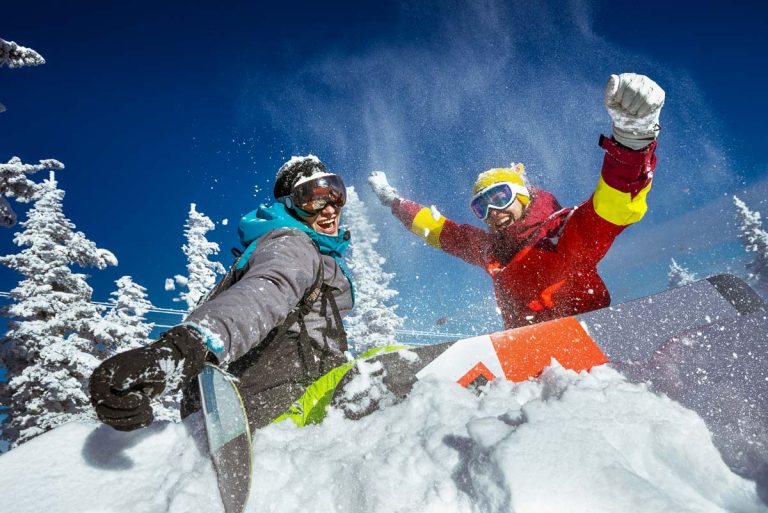 Happy couple of snowboarders having fun tossing snow and smiling