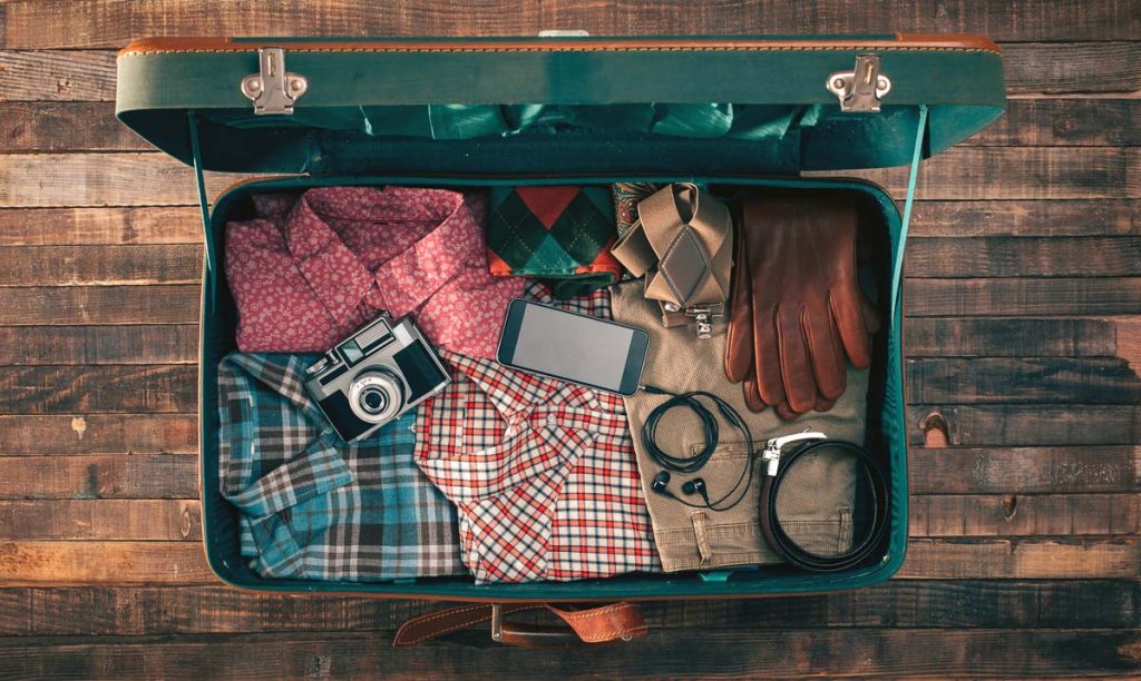 Vintage hipster traveler packing, open suitcase on a wooden table with clothing, camera and mobile phone, top view