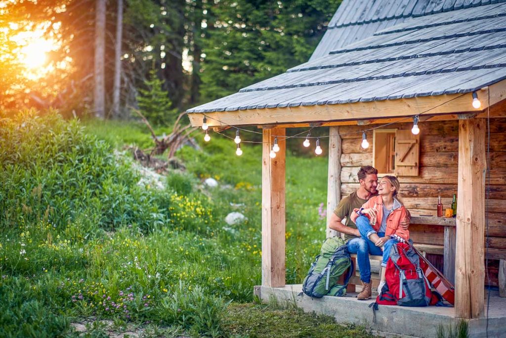 Smiling couple drinking in front of wooden cottage on the terrace.