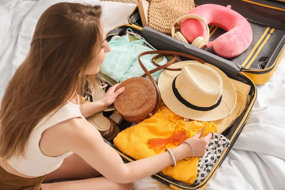 Young woman unpacking her beach accessories from suitcase in bedroom packing suitcase