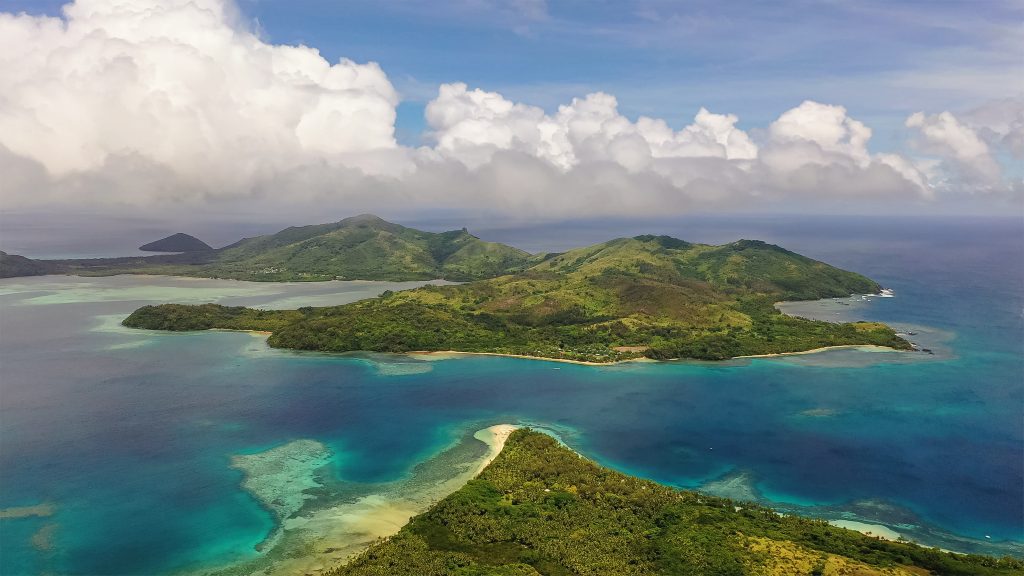 Tropical Fiji island with palm trees and clear blue-green water with white sand. Cloudy seascape